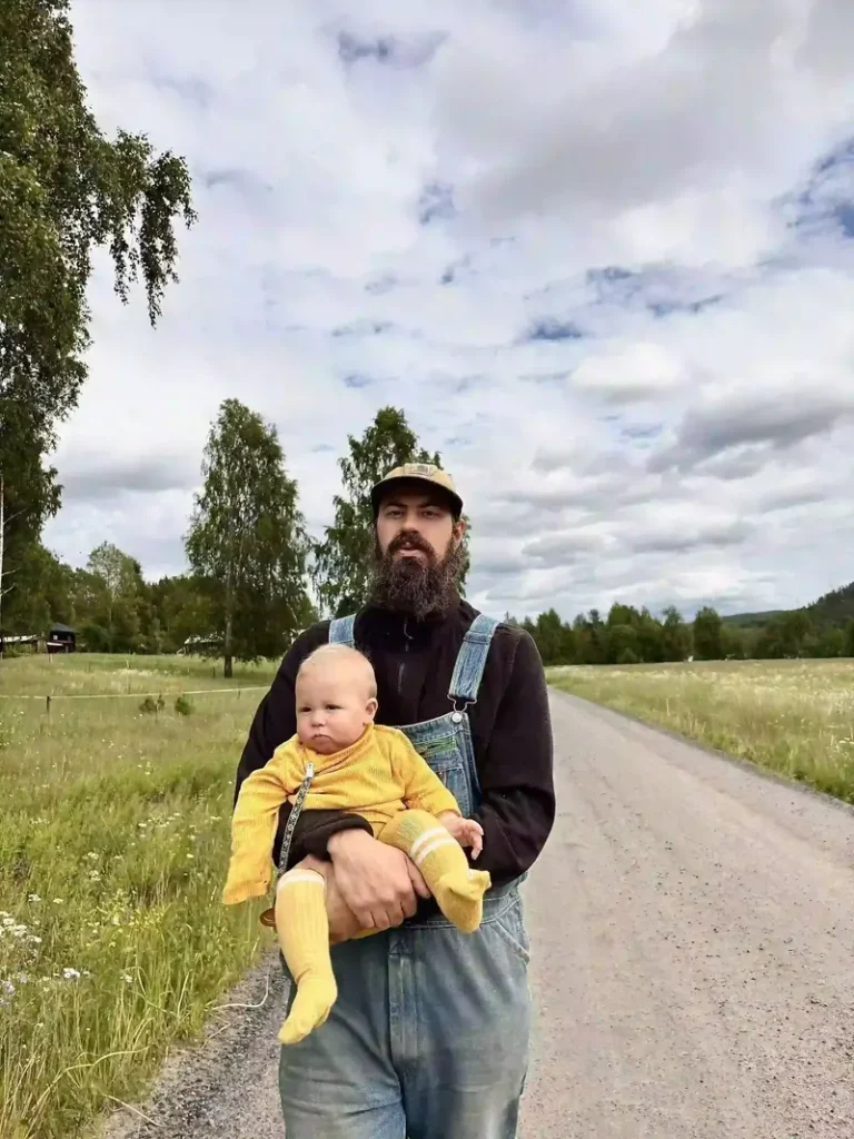 OP i snickarbyxor håller sitt barn i famnen på en grusväg på landsbygden, från blogginlägget om att bli hiphop-bonde.
