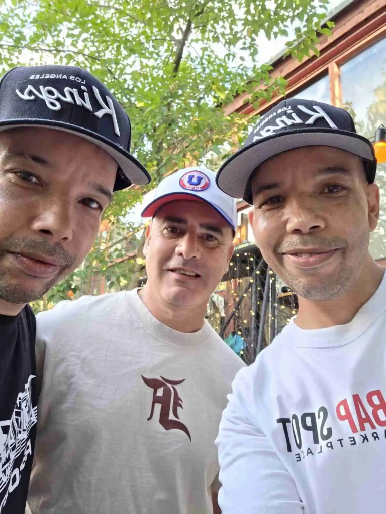 Ramo och Thabo från AFC i kepsar tar en selfie med Miguel utomhus på Årstabo.