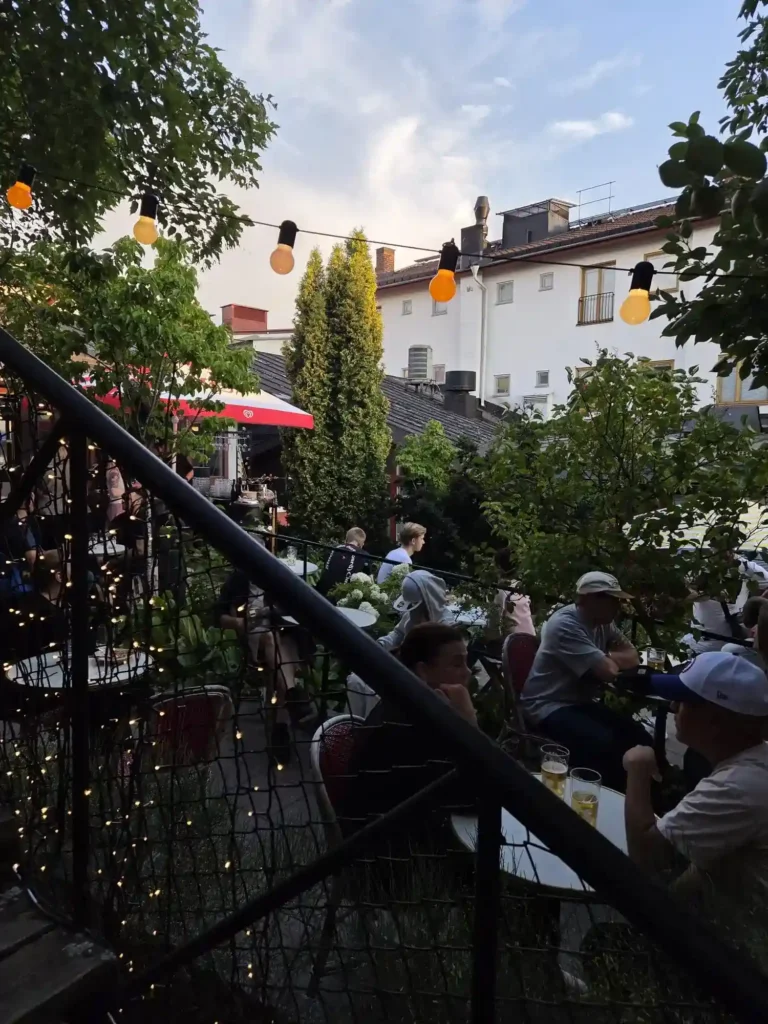 Besökare sitter vid borden under ljusslingor på Årstabos lummiga innergård.