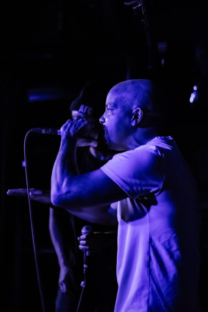 Hiphopduon AFC uppträder live på scen i lila scenbelysning med mikrofoner i hand.