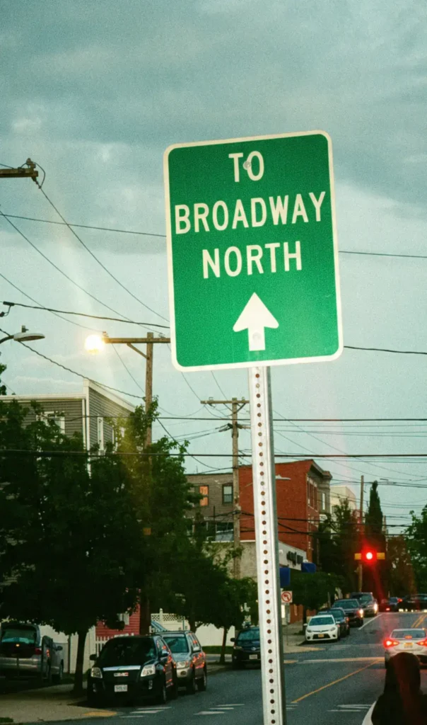 Grön vägskylt med texten To Broadway North vid en gata