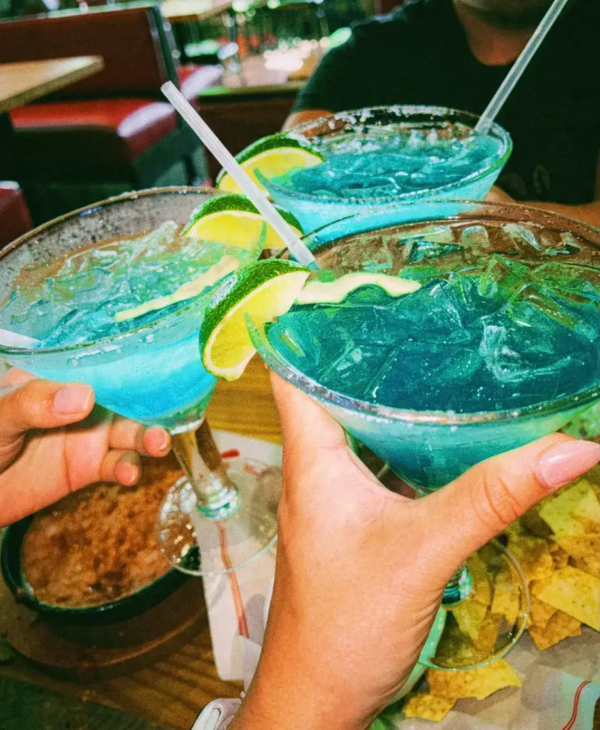 Tre blå margaritas i glas som skålas över ett bord på restaurang