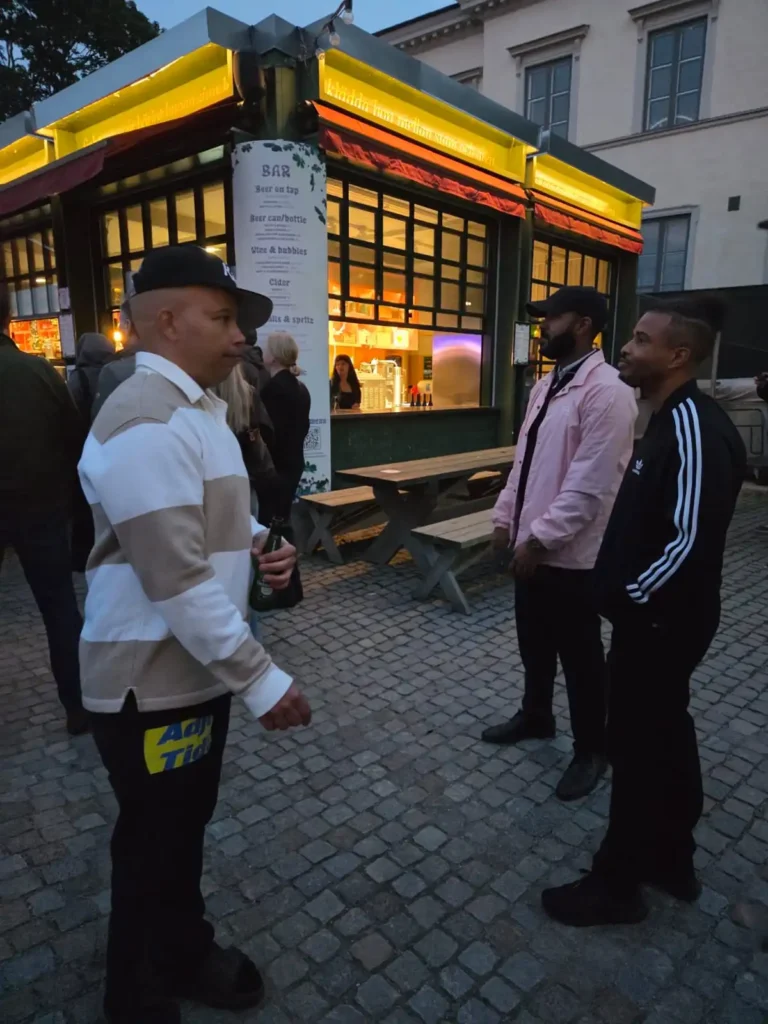 Ramo från AFC i randig tröja och Erik Lundin i svart Adidas-jacka pratar utomhus på Mosebacke terrass. – Boom Bap Spot