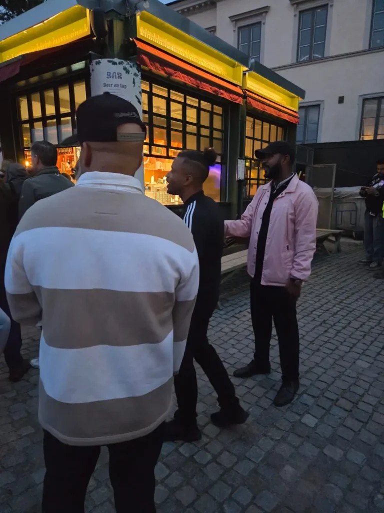 Erik Lundin iklädd svart Adidas-jacka pratar med gänget utomhus vid baren på Mosebacke. – Boom Bap Spot