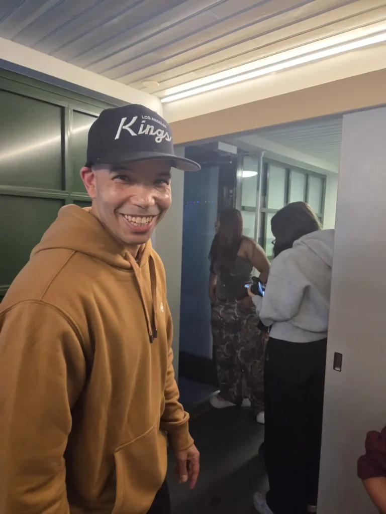 Thabo från hiphopduon AFC iklädd brun hoodie och LA Kings-keps ler mot kameran i logen bakom scenen på Mosebacke. – Boom Bap Spot