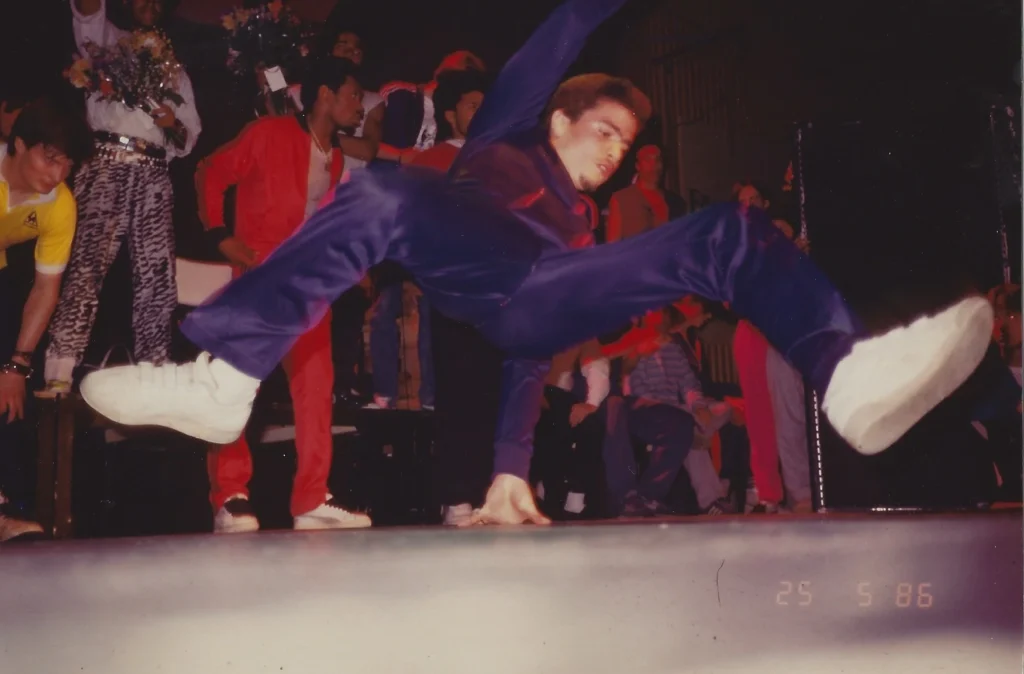Icey Ice doing flying footwork breakdance-move on 2 Def Days of Hip Hop festival in Stockholm 1986, in front of audience on stage. Mr Wave in the bavckground.