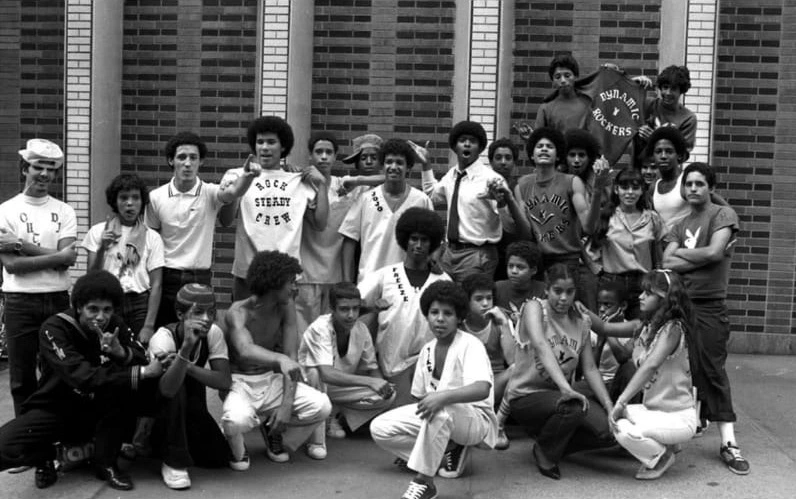 Svartvitt fotografi av Rock Steady Crew och Dynamic Rockers, med Corey sittandes bakom Take One.